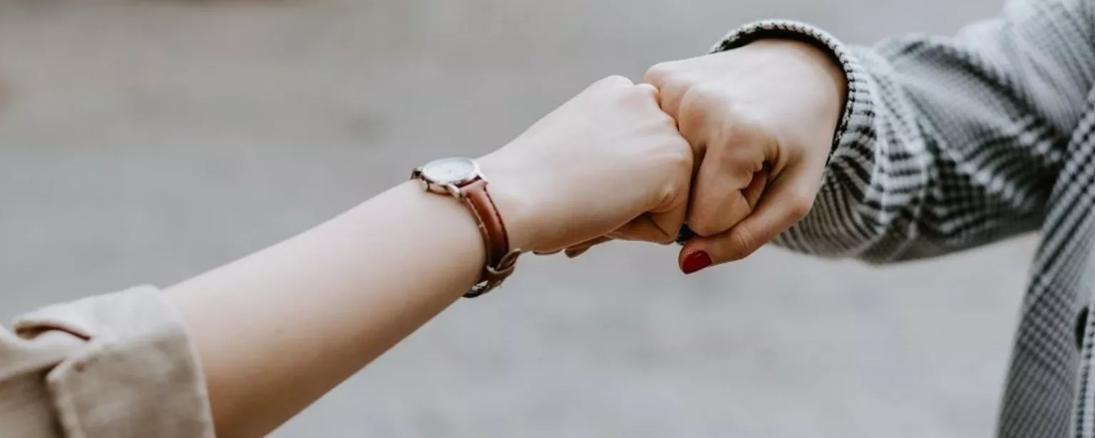 Hände zweier Frauen im Business-Outfit beim Faustgruß (Fist Bump)