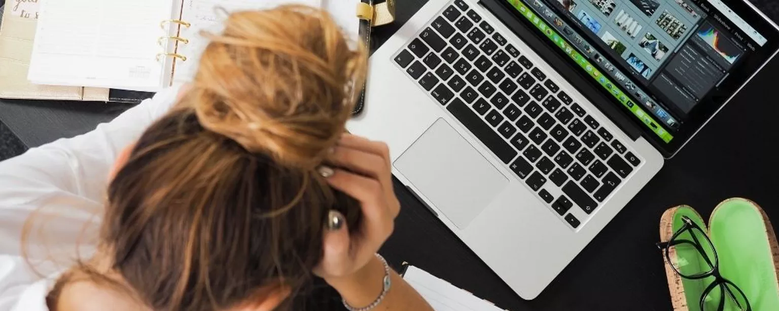 Junge Frau sitzt vor einem Laptop und stützt den Kopf in die Hände