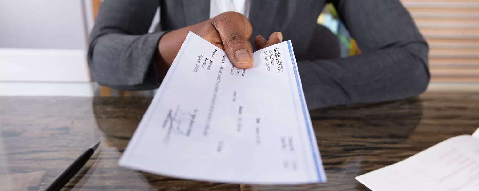 A payroll employee presents a paycheck, with the focus on a hand holding the check.