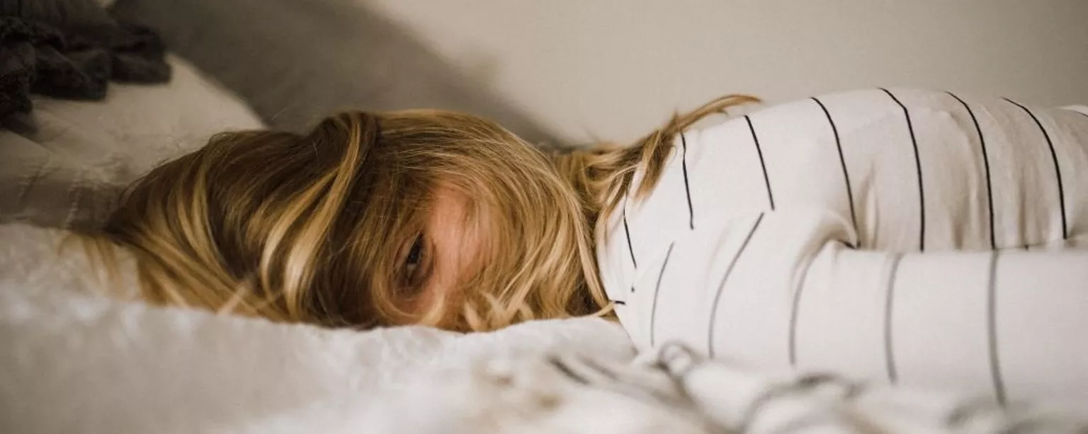 Erschöpfte Frau liegt voll bekleidet mit offenen Augen auf einem Bett
