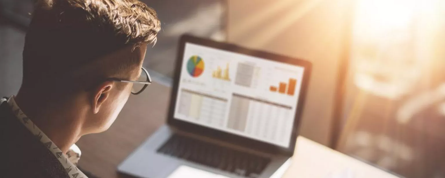 Man sitting at a desk looking at charts on papers and a computer screen.