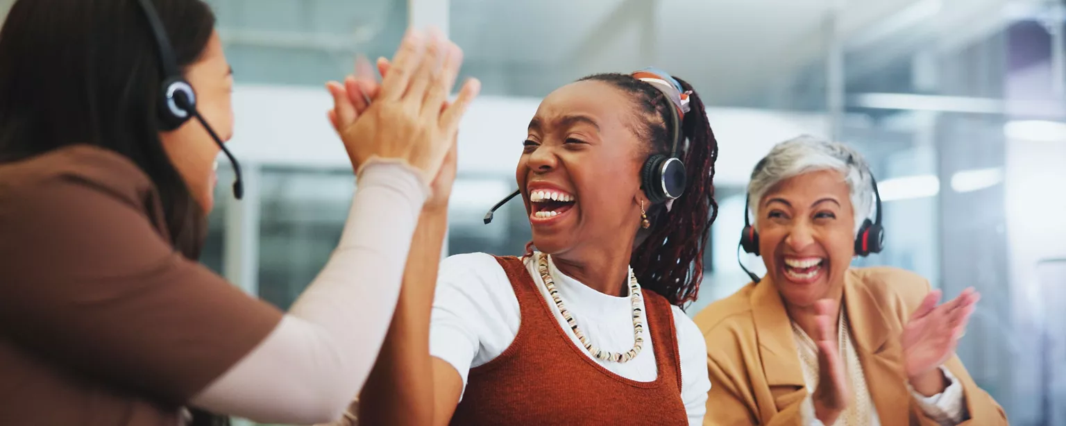 Customer service team members wearing headsets laugh and celebrate together with a high-five and applause.