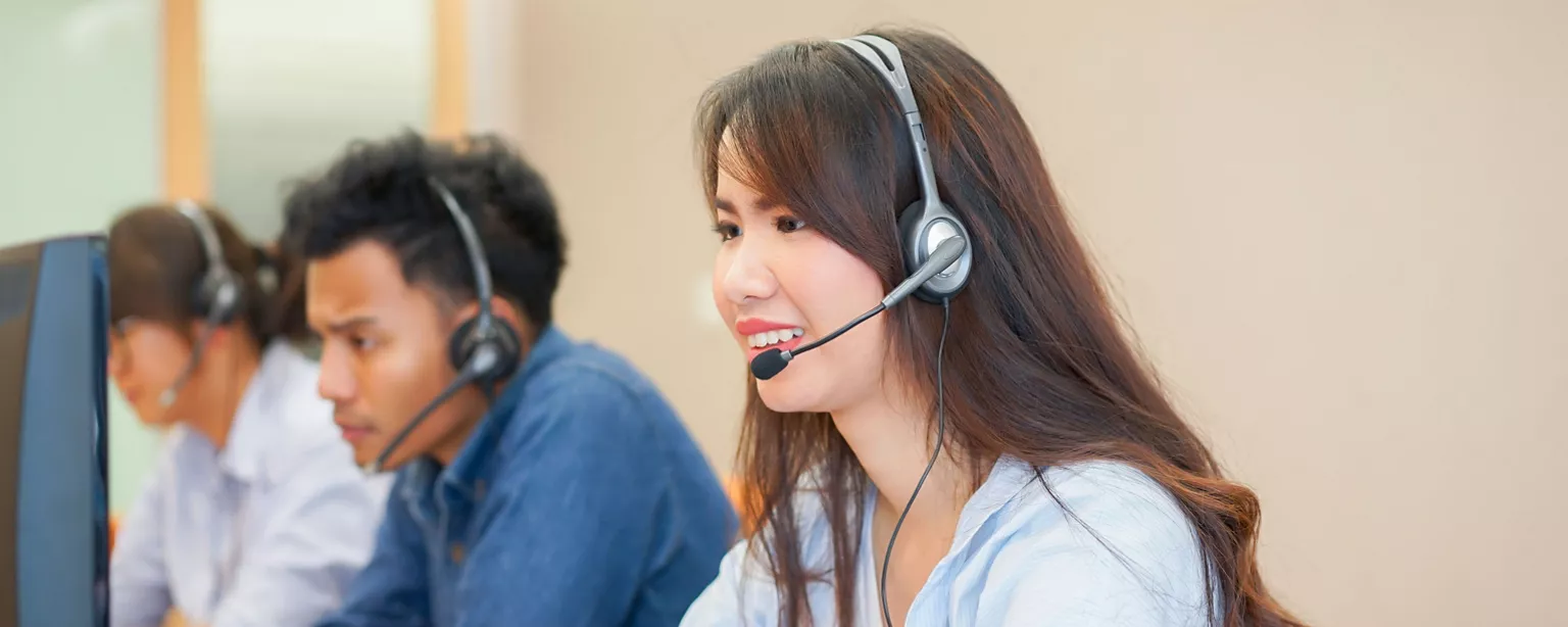 A woman wearing a headset works next to colleagues in a call center that provides customer support.