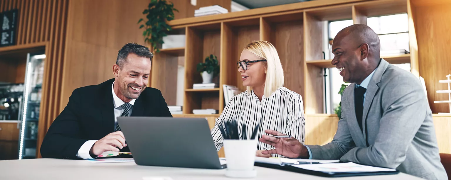 Three people working in the legal profession smile and talk while sitting at a table in a legal office.