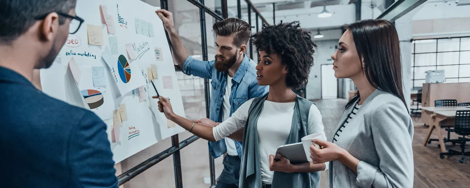 Diverse employees in a marketing and creative department gather near a white board for a brainstorming session.