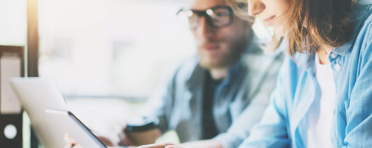 A woman and man at work looking at a tablet.