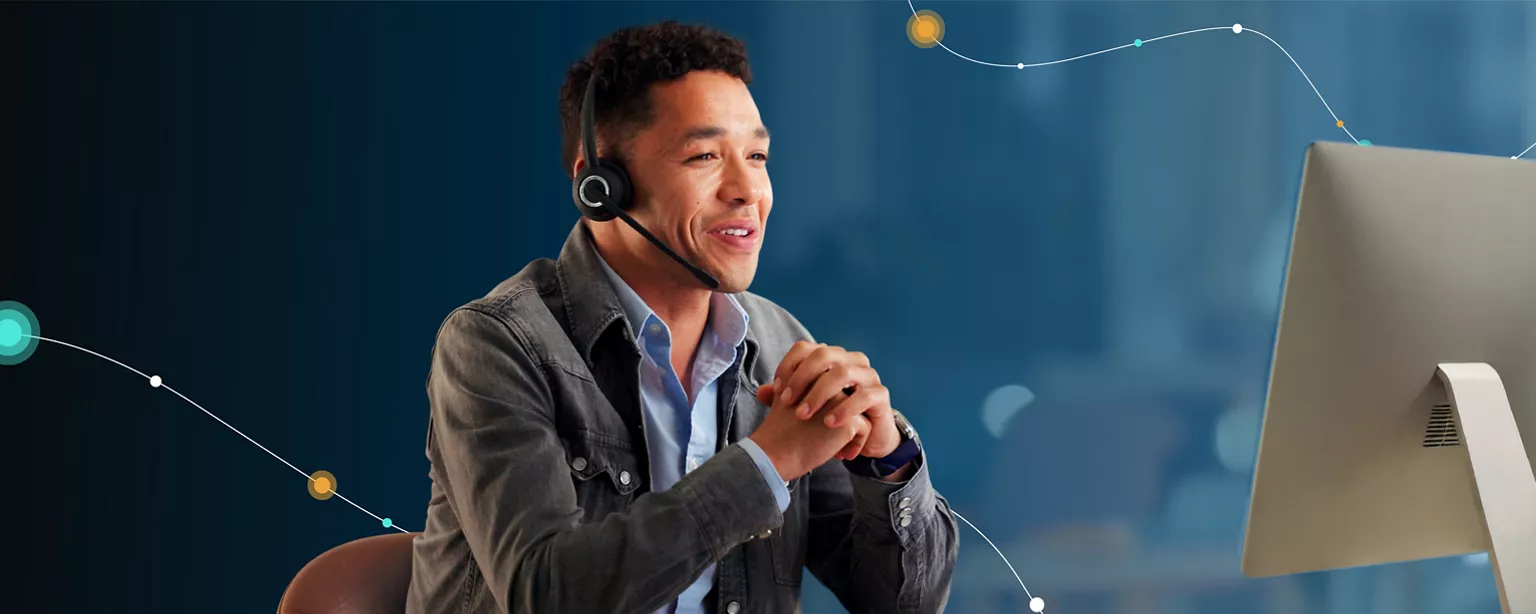A man wearing a headset works at his laptop while providing customer support to someone over the phone.