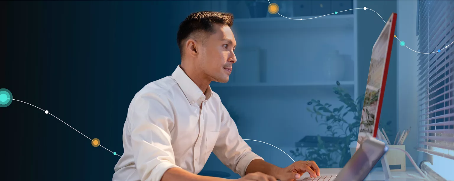 A man in a white dress shirt and tech and IT environment sits at a desk and stares a monitor.