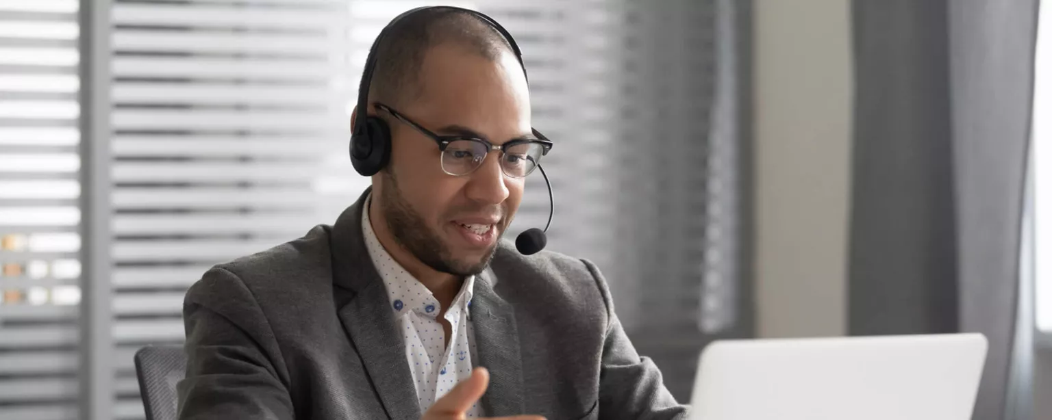 A man wearing a headset talks as he looks at his computer screen.