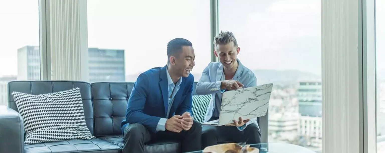 Dois homens no trabalho rindo com um computador na mão
