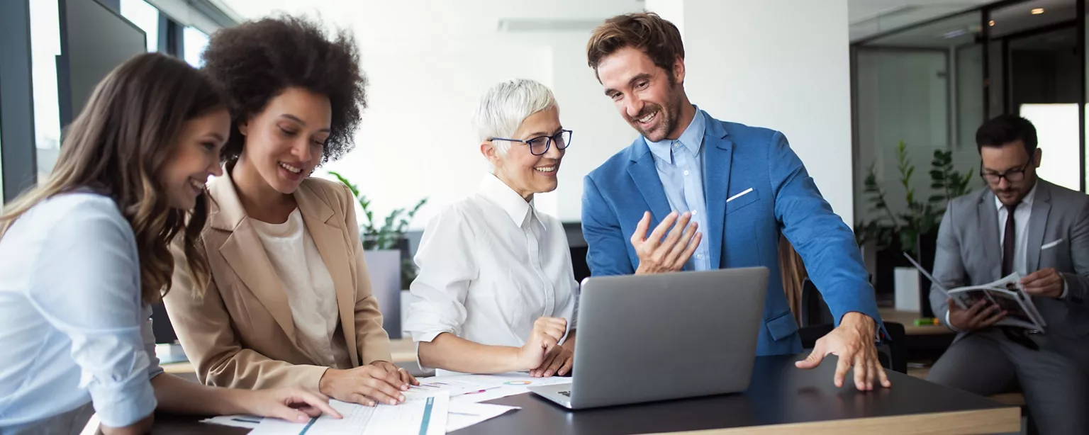 A team of business professionals reviews data and discusses technology upgrades around a laptop.