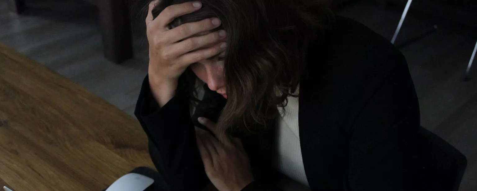 Female boss sits in front of a laptop looking stressed with head in hands