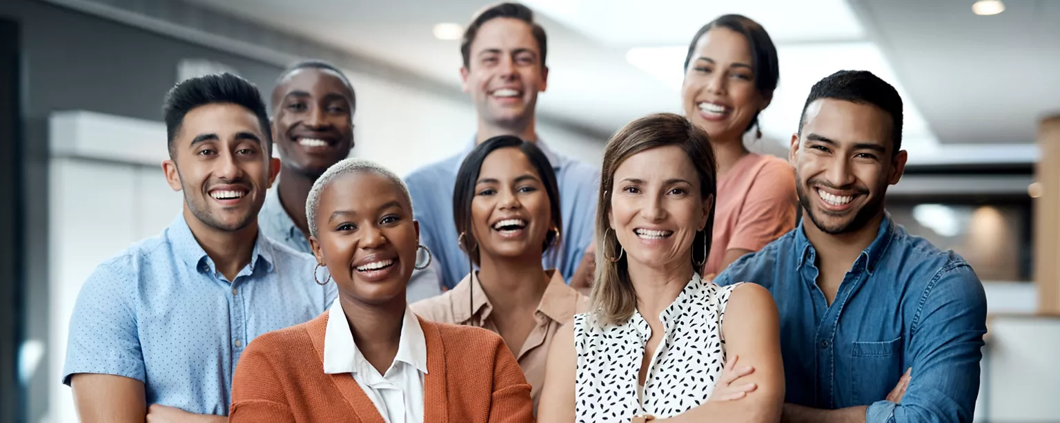 A diverse group of employees stand together and smile in an office conference room.