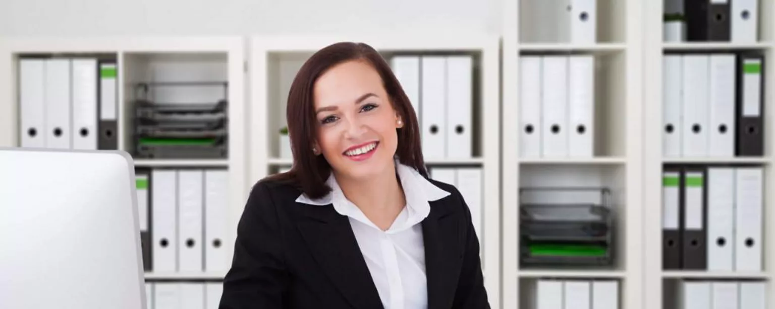 Woman working with calculator in front of shelves of notebooks