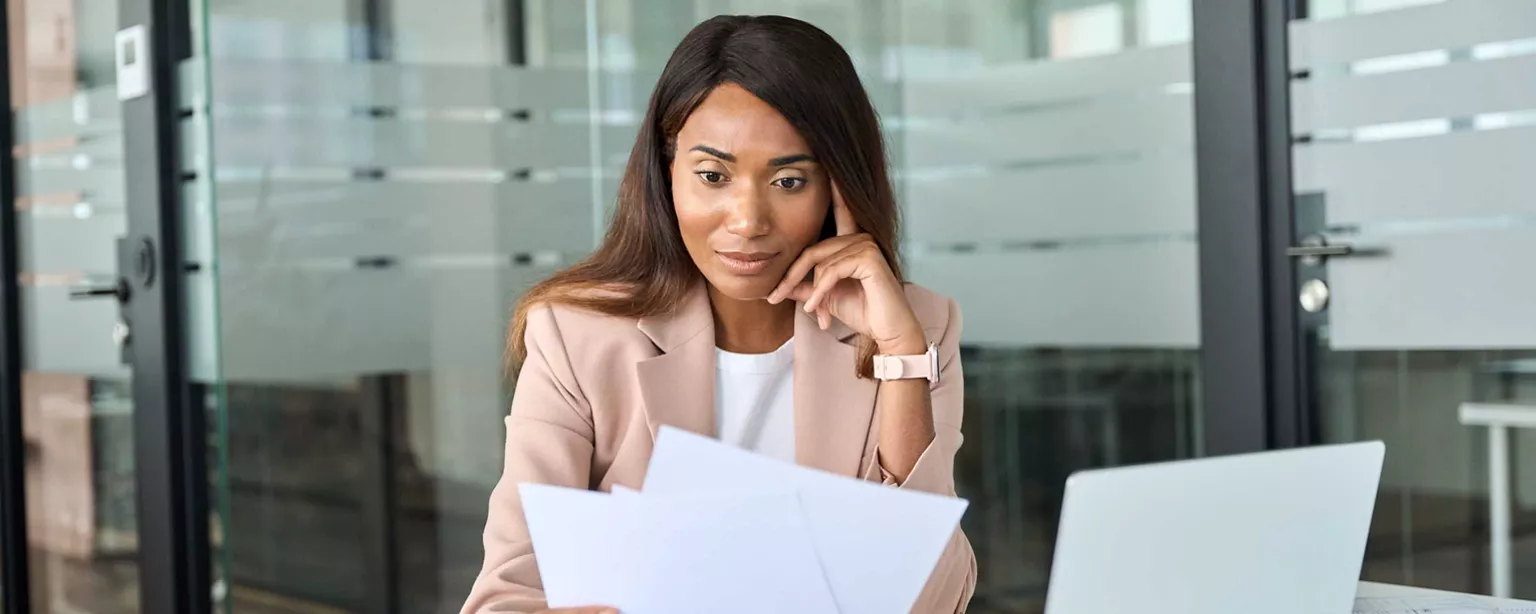 A professional woman thoughtfully reviews documents at her desk in a modern office, reflecting on hiring decisions.