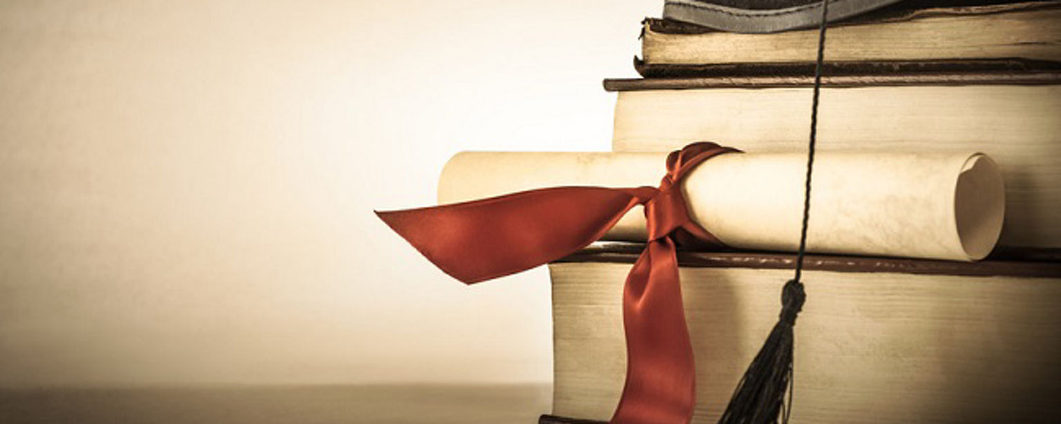 A mortarboard and graduation scroll, tied with red ribbon, on a stack of old battered book with empty space to the left.  Slightly undersaturated with vignette for vintage effect.