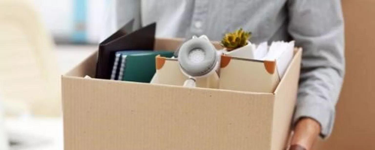 Employee carries box full of desk items after being fired from their creative job