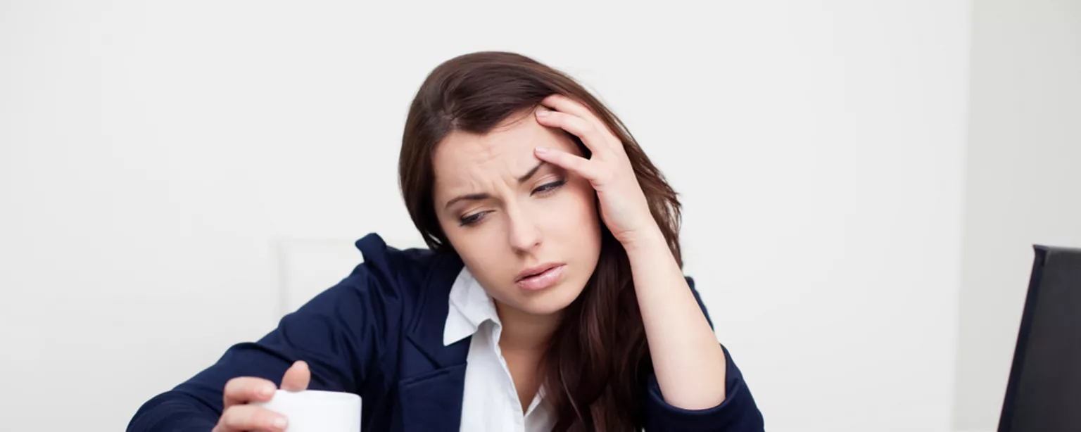 What to Do When Calling in Sick is Unavoidable — woman at a desk holding a tissue with one hand on her head