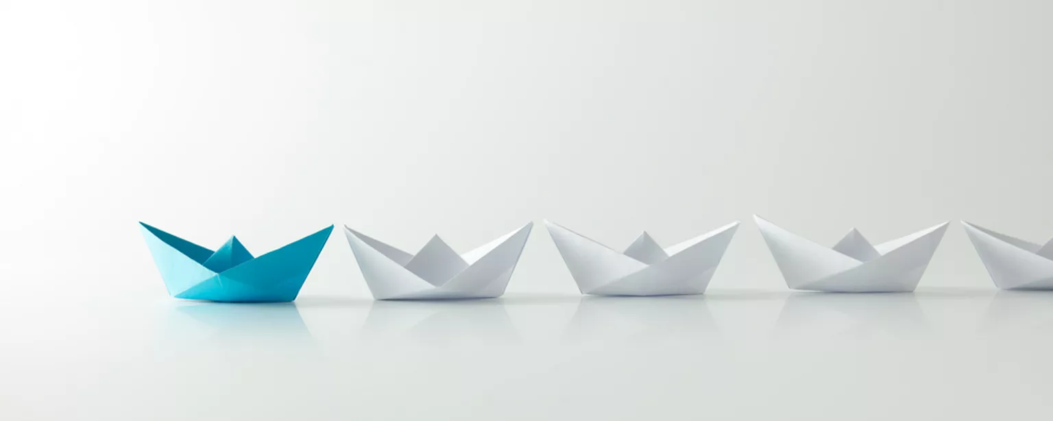 White paper ships in a line with a blue one in the lead.