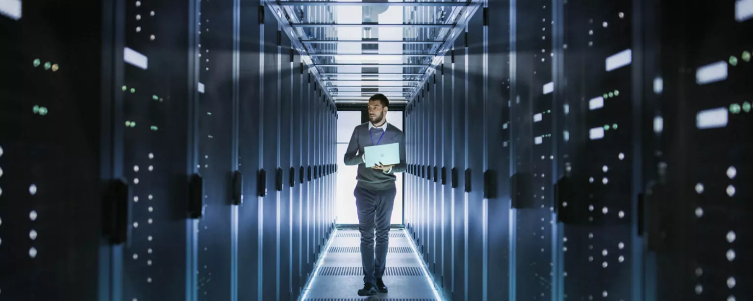 A man carrying a laptop walks down a hallway lined with futuristic light panels.