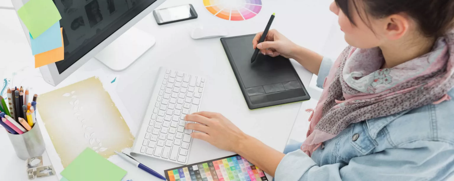 Woman at her desk using computer and drawing pad.