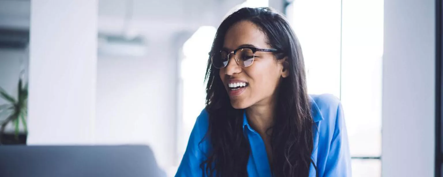 Une femme souriante assise à un bureau devant un ordinateur portable.