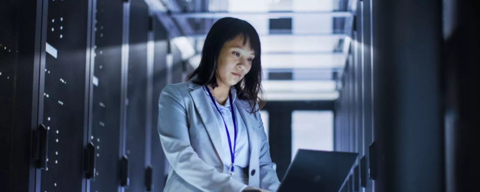An IT Business Systems Analyst reviews data with a bank of servers nearby.