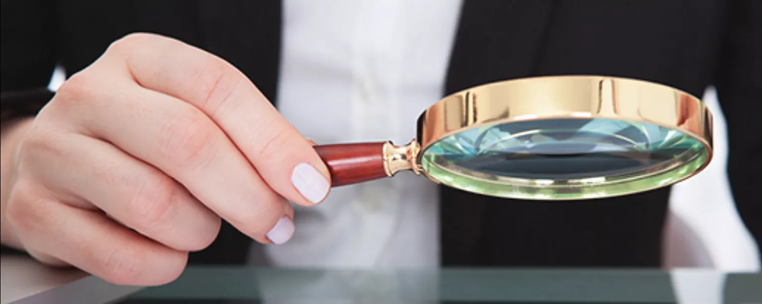Hot Jobs: What Does It Take to Be a Compliance Manager? — hand holding magnifying glass