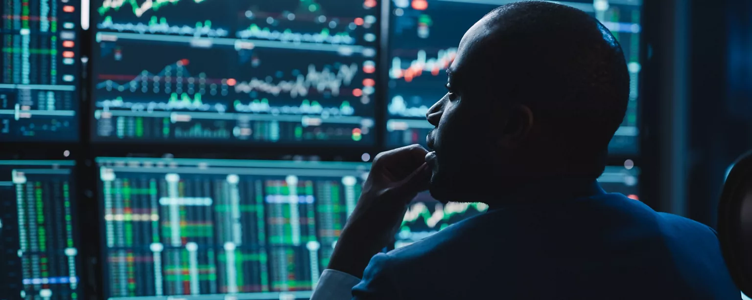 Financial professional reviewing market data and charts on multiple computer screens.