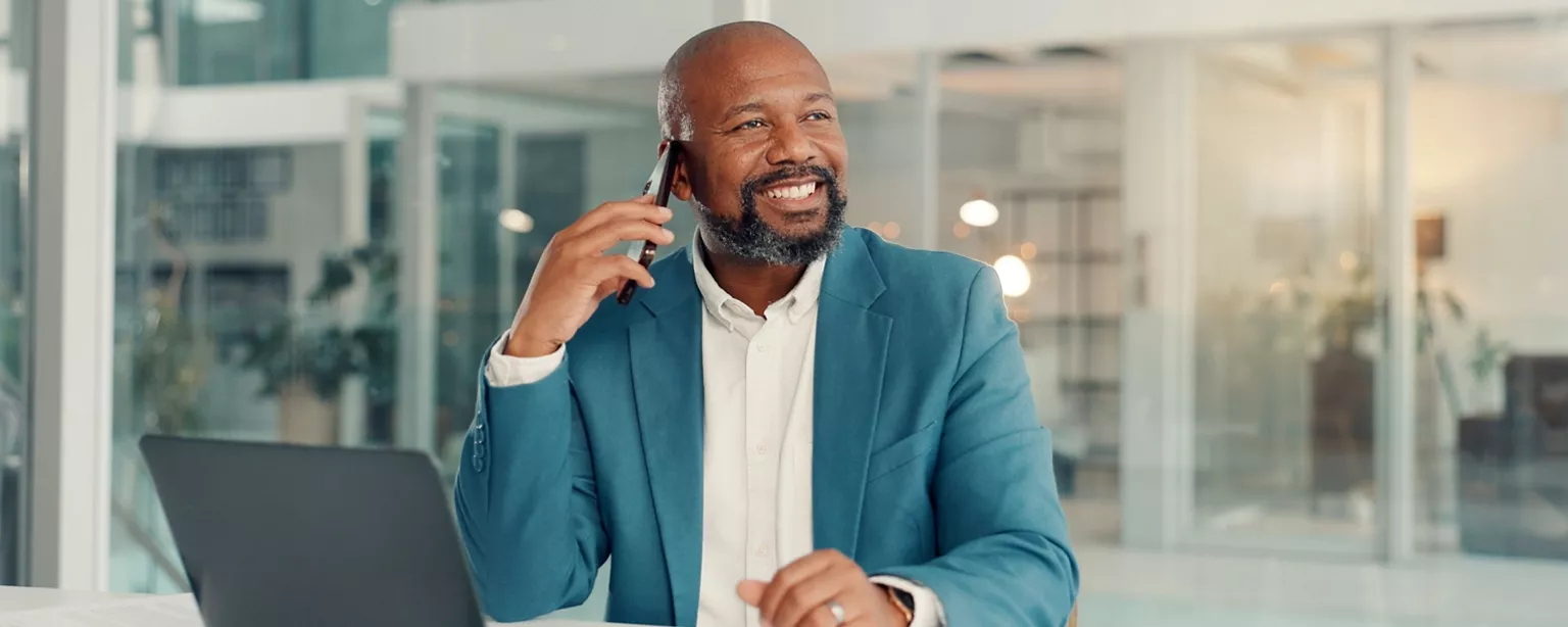 Professional in an office setting reviewing information on a laptop while speaking on a phone.