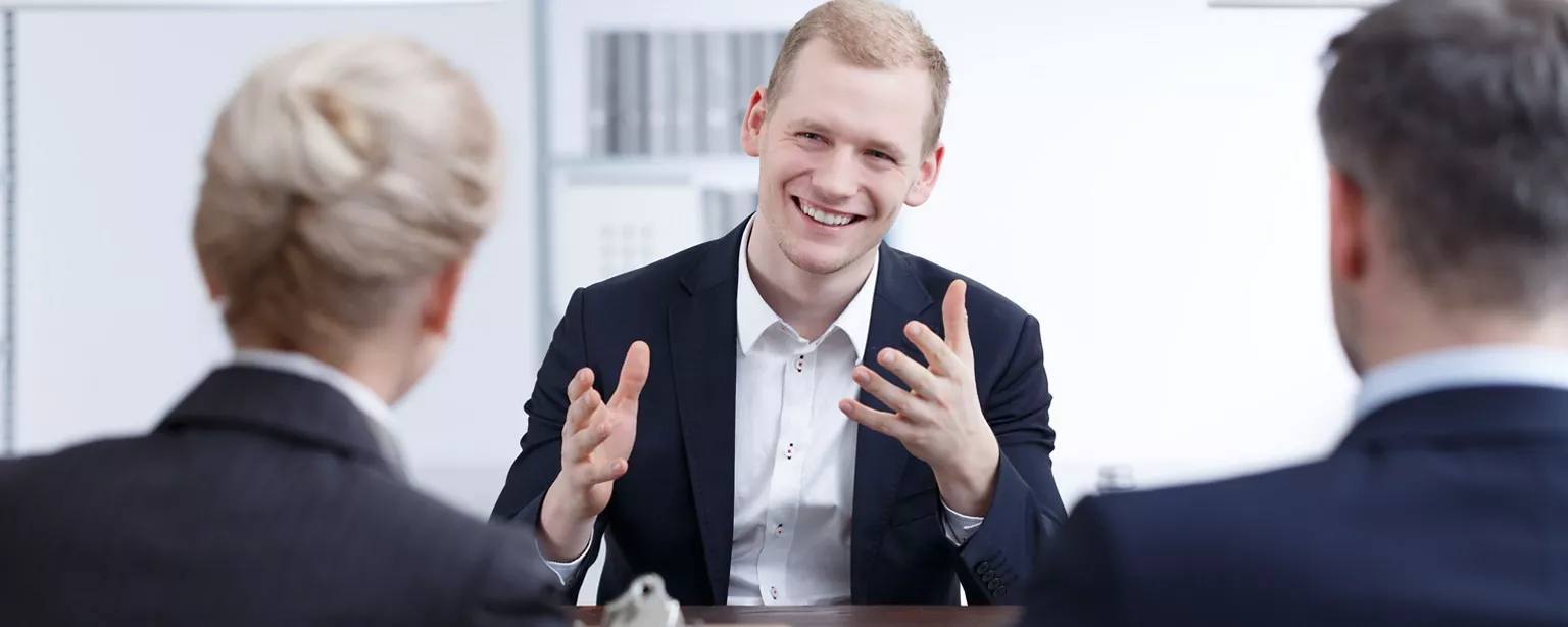 A candidate smiles as he responds to "tell me about yourself" during a job interview. 