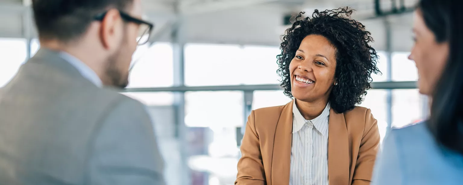 A professional woman smiles confidently during a job interview with two interviewers.