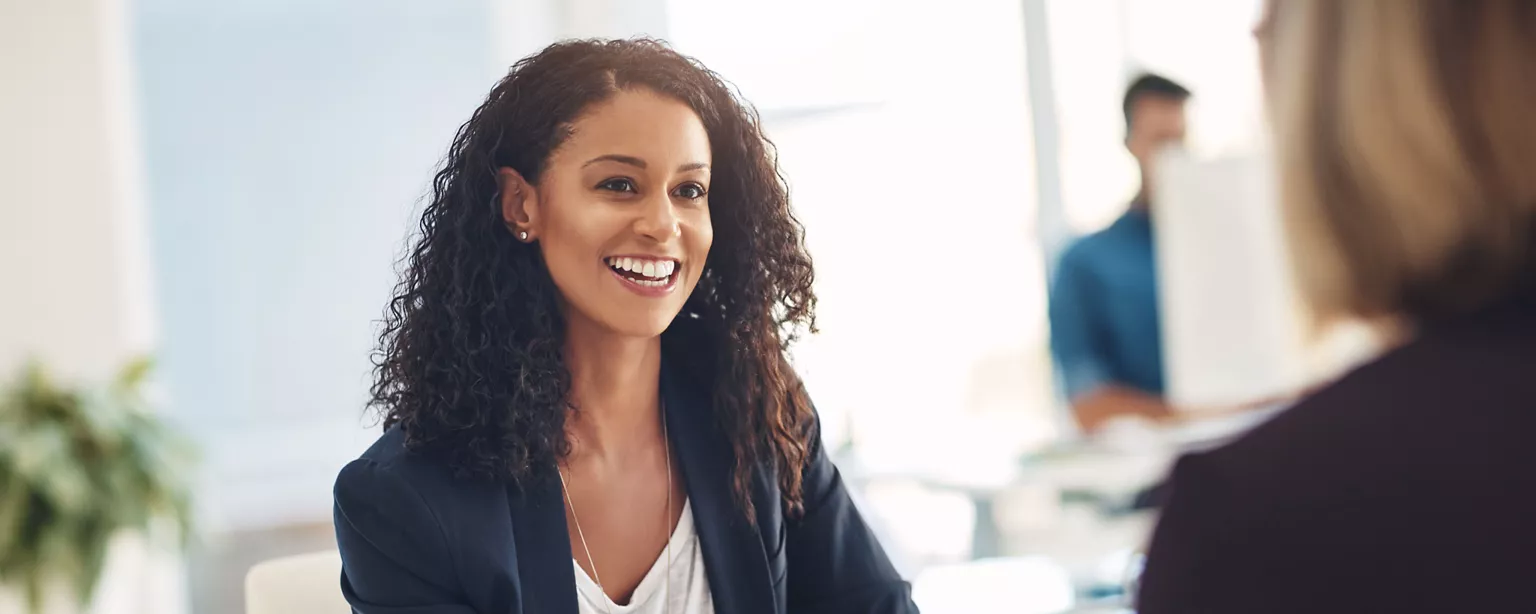 A confident, professional woman smiles during a job interview while she answers the question, "Why should we hire you?"