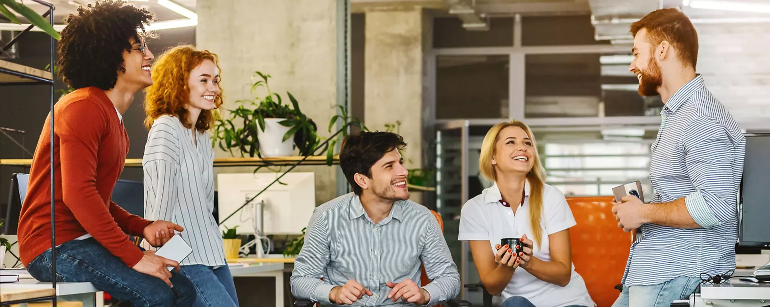 A group of colleagues laughing and having a casual conversation in a modern office.