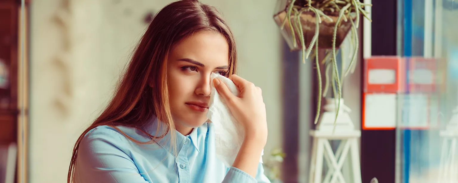 A woman in a light blue shirt wipes away tears while sitting at a table.