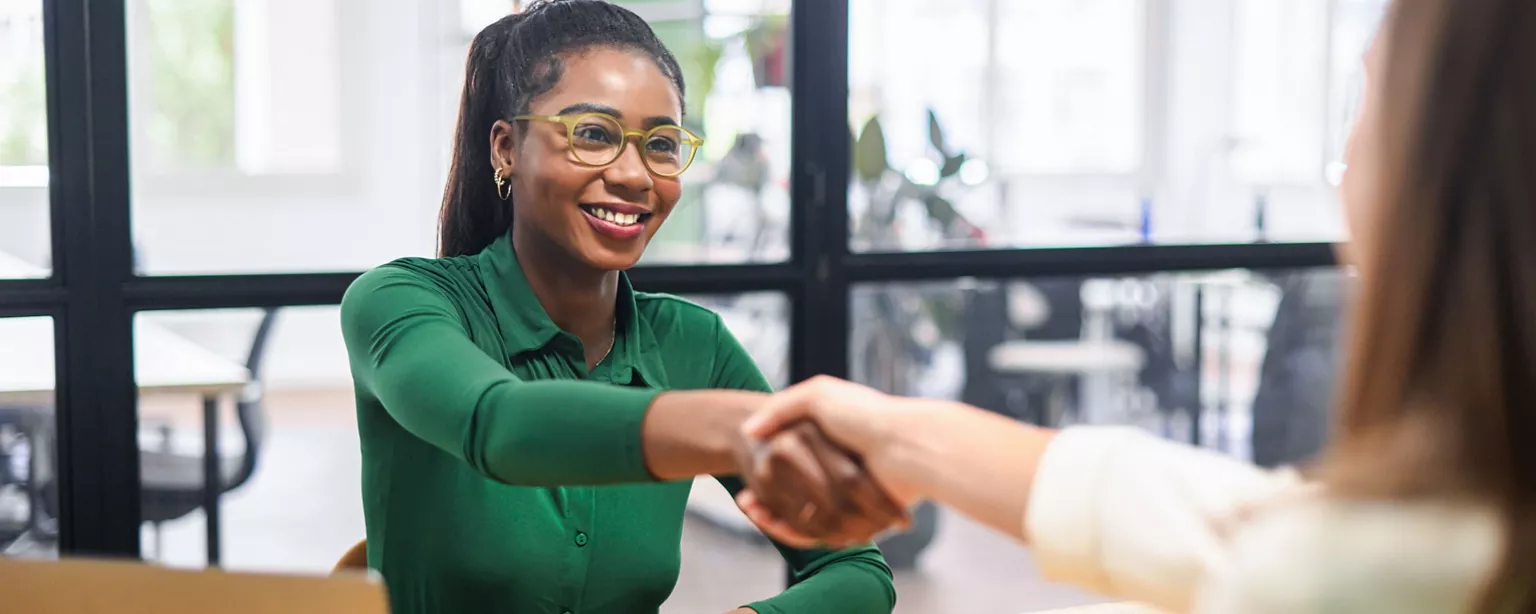 A hiring manager and a job candidate close an interview with a handshake.