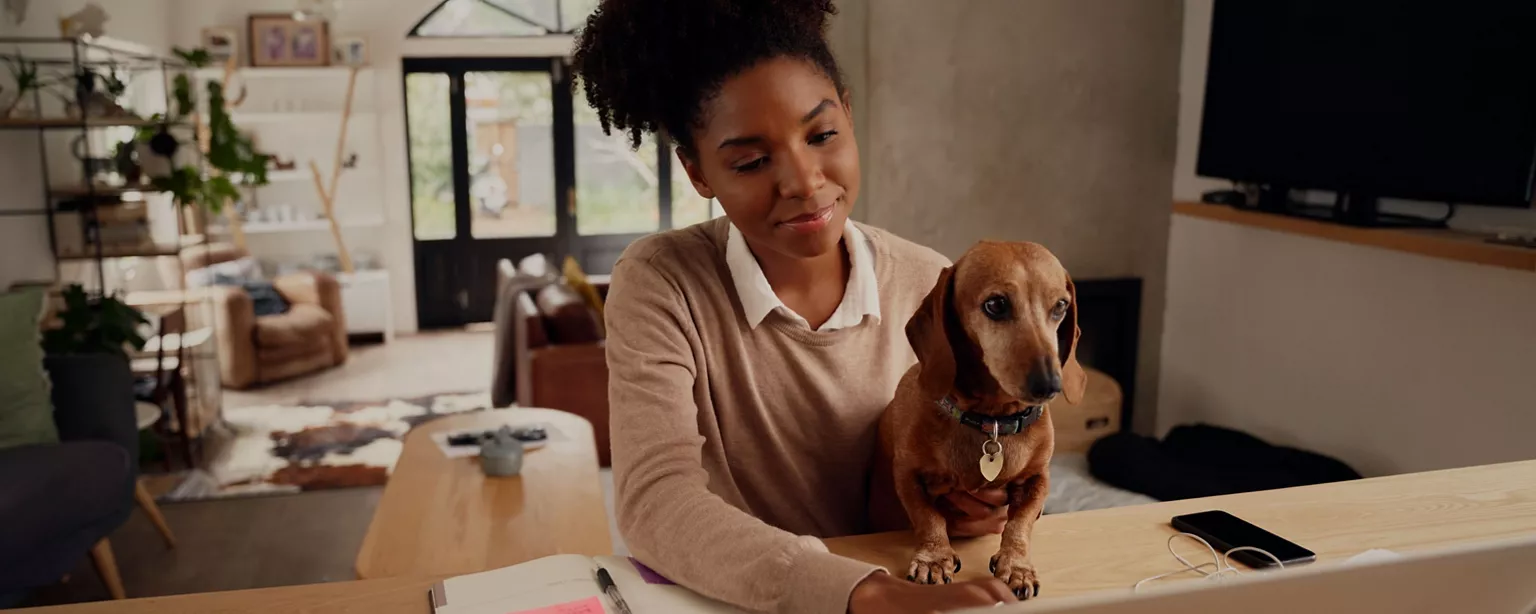 A woman works remotely from home as her dog sits on her lap and looks at the computer screen, too.