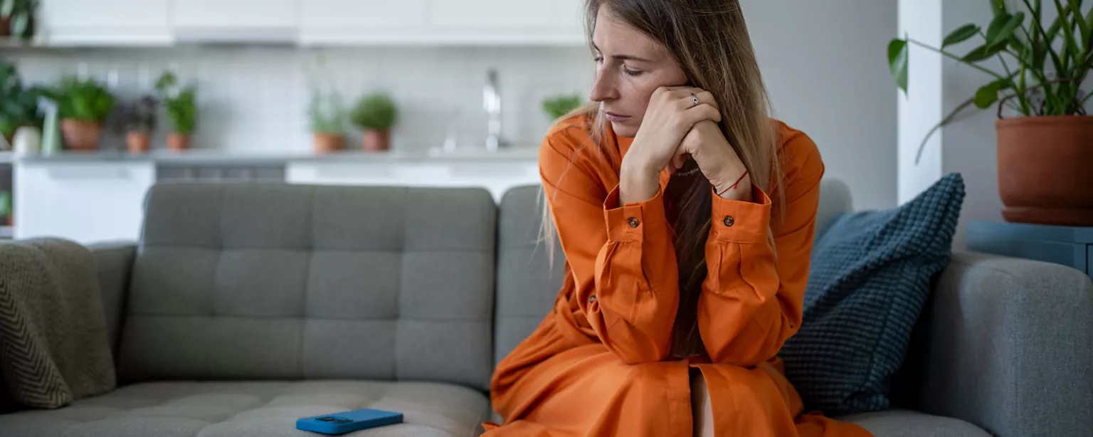 A job seeker looks at her phone on the couch, wondering if she should follow up after applying for a job.