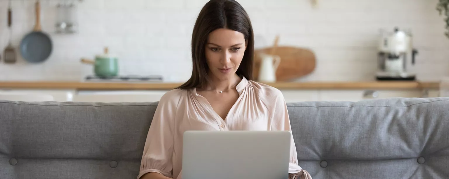 A woman sits on her couch and types on a laptop as she follows up on her job application by writing an email.