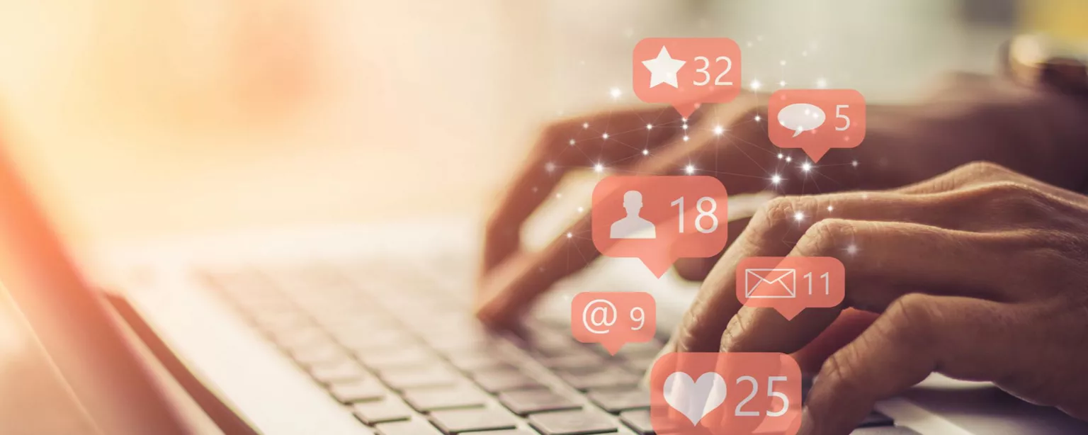 Hands typing on a laptop, with social media-type images floating above, such as a chat bubble and a star.