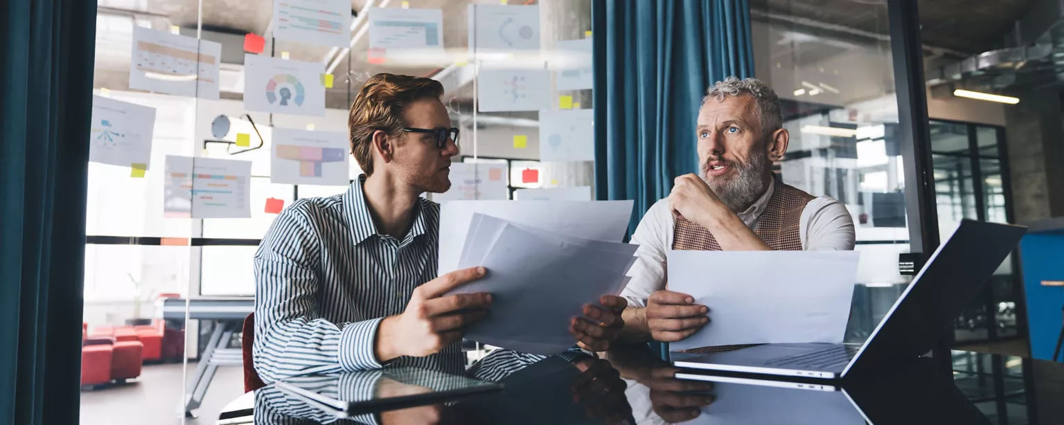 Two colleagues from different generations review documents together in an office.