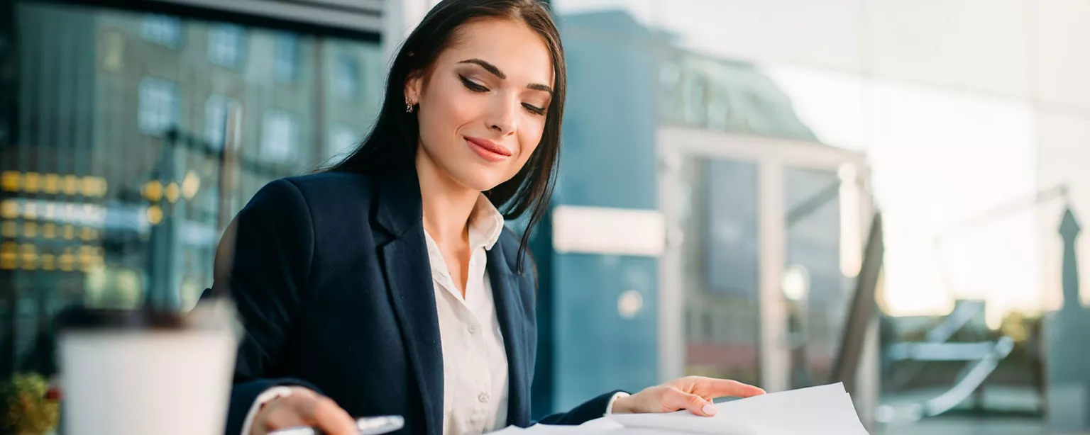 A compliance attorney reviews her notes as she works outdoors with buildings in the background.