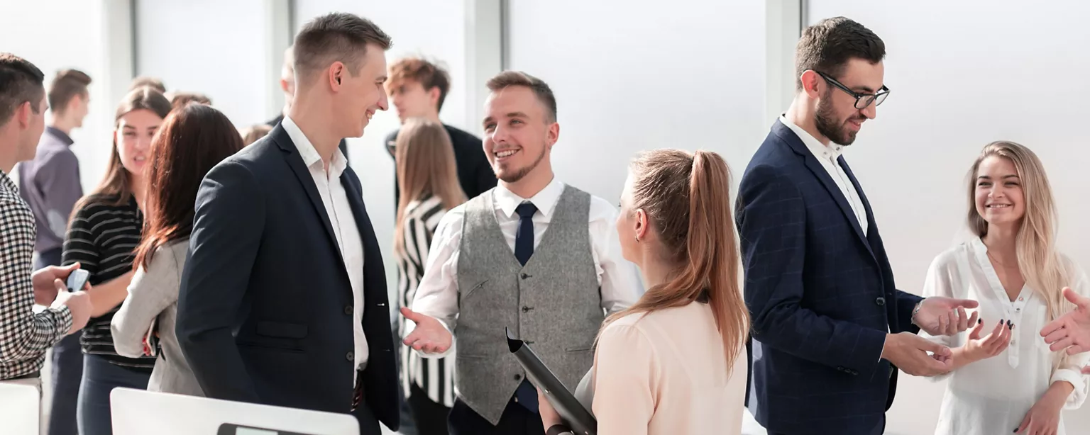 A group of professionals participate in a networking event, smiling while making conversation in a bright, open conference hall.