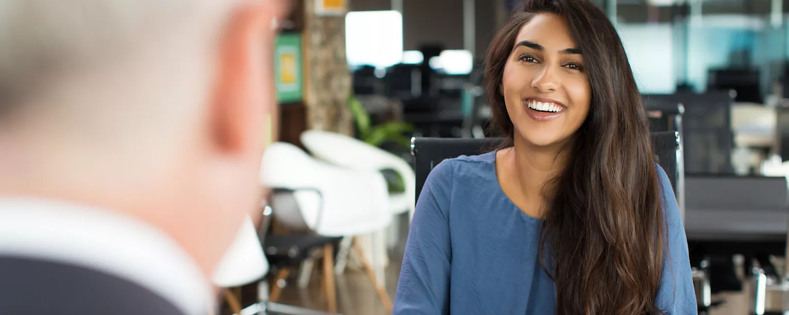 A smiling and confident young woman sits across from a hiring manager at a desk.