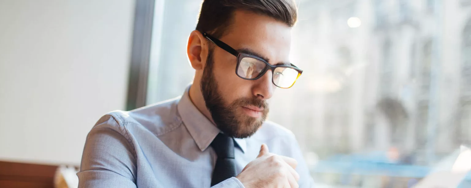 A man at an office desk holds a pen while reviewing a resume.