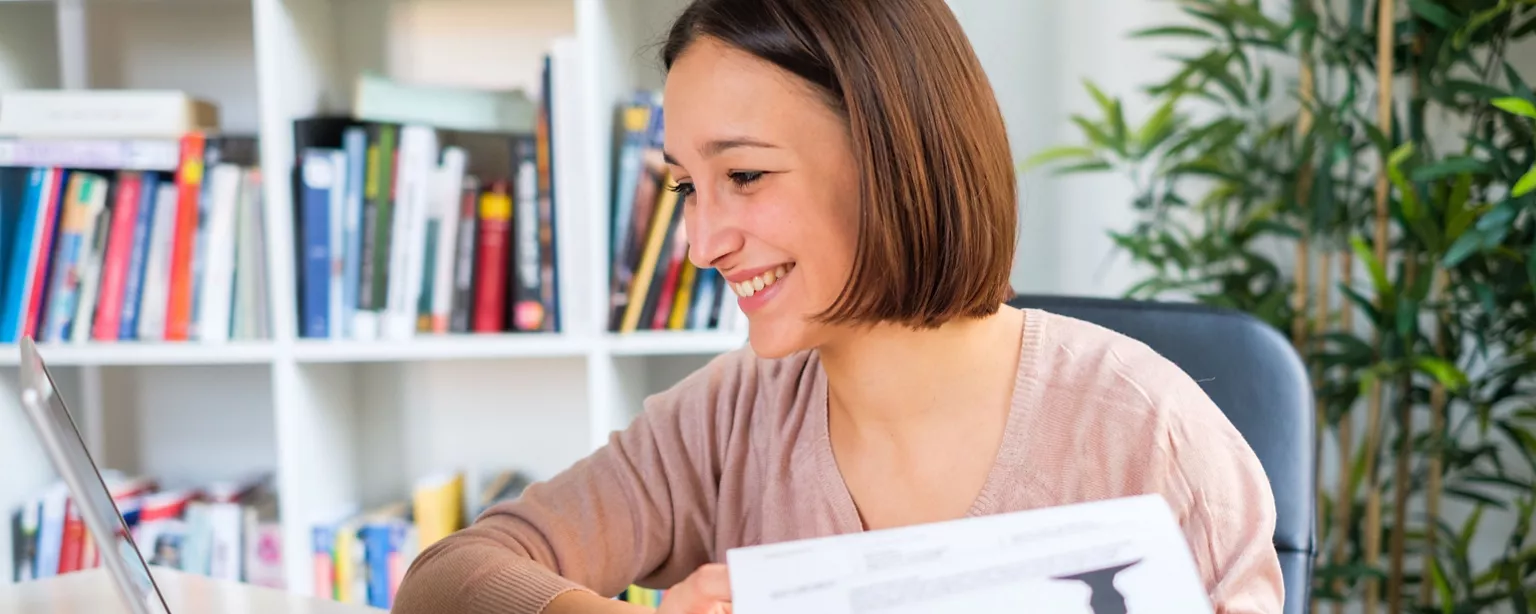 A woman smiles as she works on her resume.