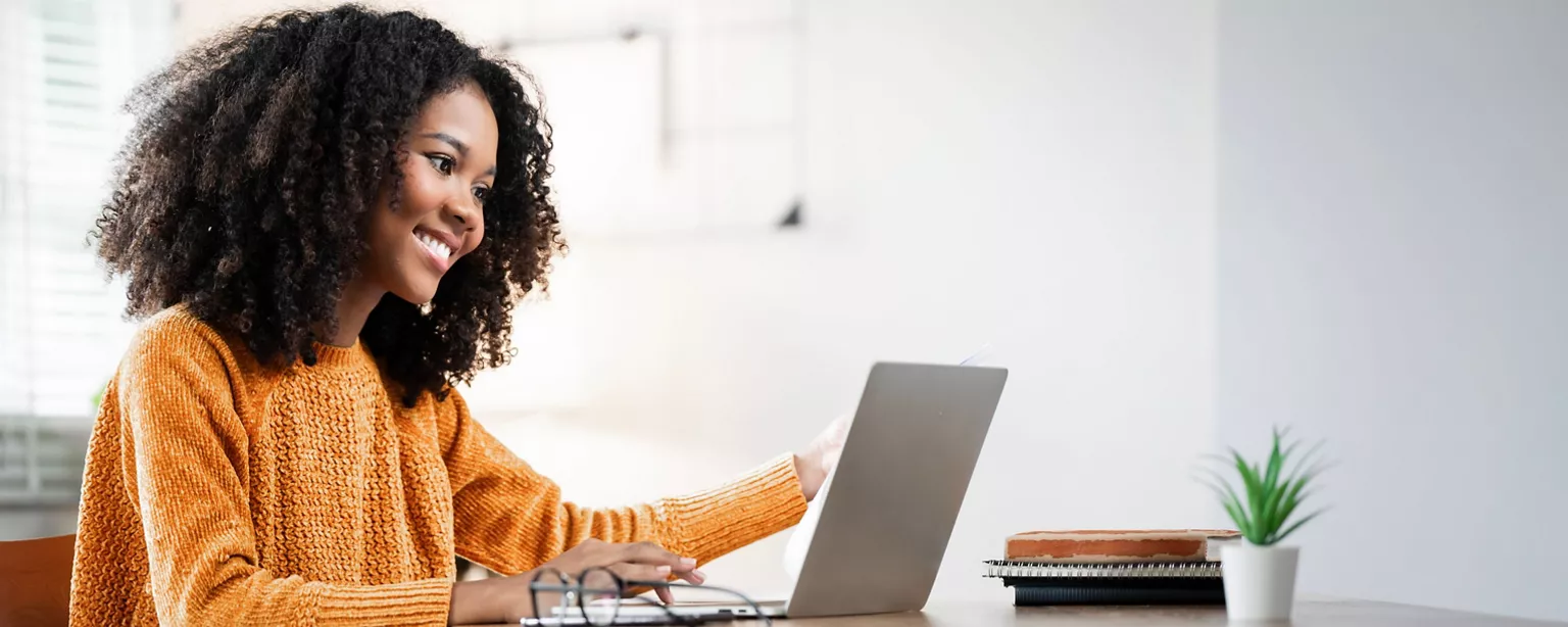 A woman smiles while replying to an email on her laptop, probably writing an email to accept an invitation for a job interview.