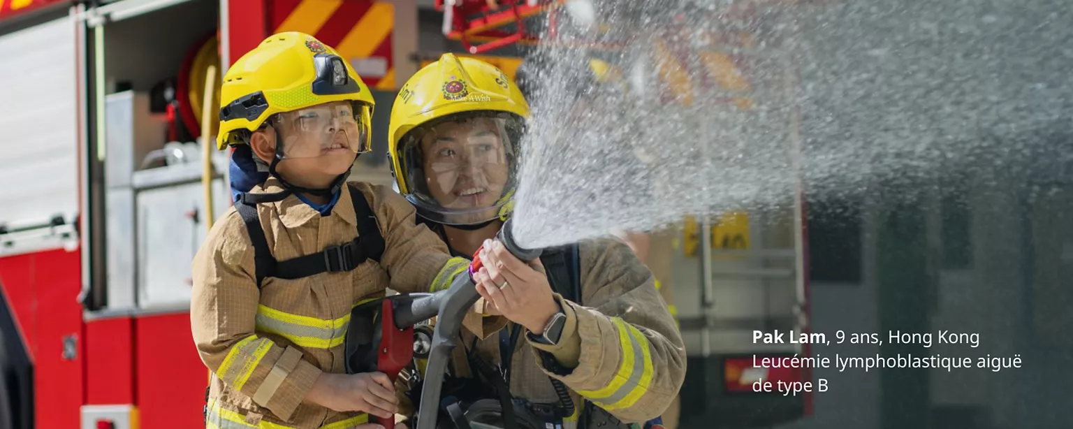 Un enfant et un pompier arrosant avec une lance à incendie, avec la légende sur l'image « Pak Lam, 9 ans, Hong Kong, leucémie lymphoblastique aiguë de type B ».