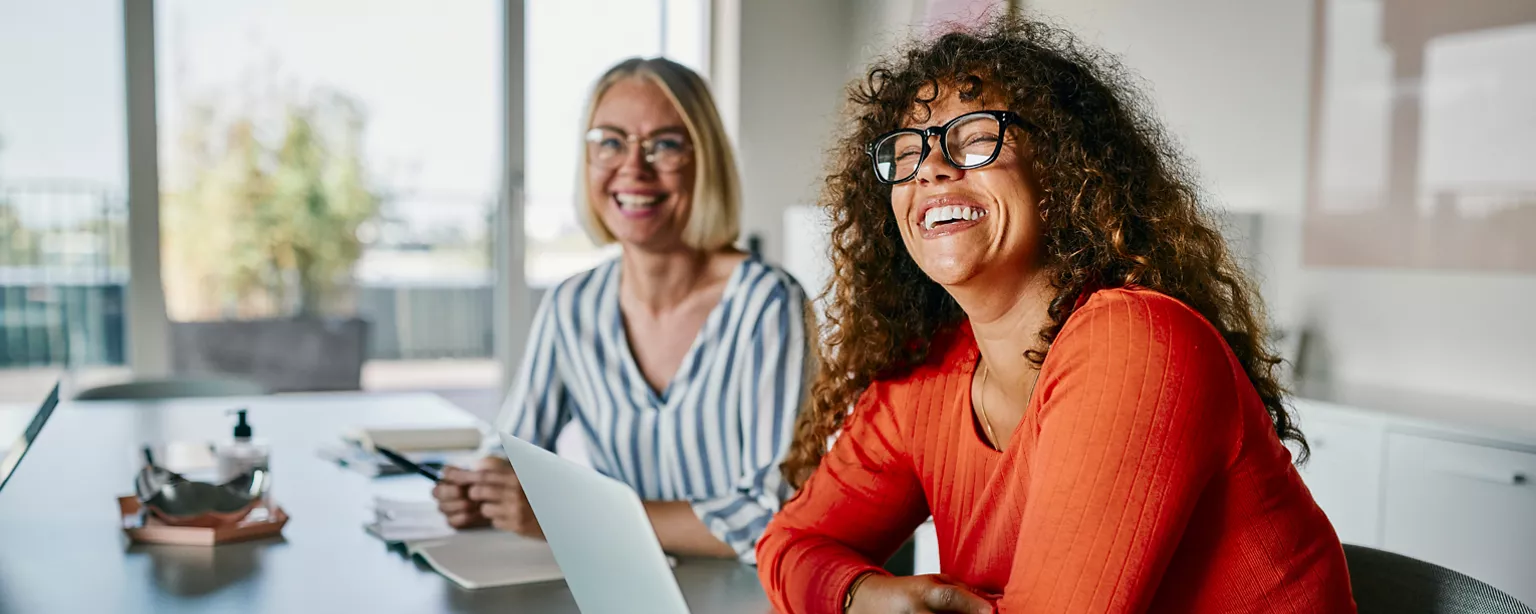 two female workers laughing at the camera in an office setting