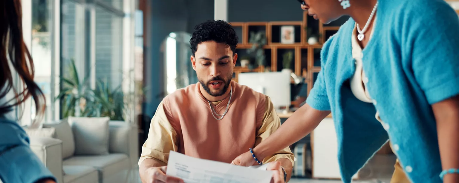 man sitting at a desk, reviewing work with other people in an office looking stressed out